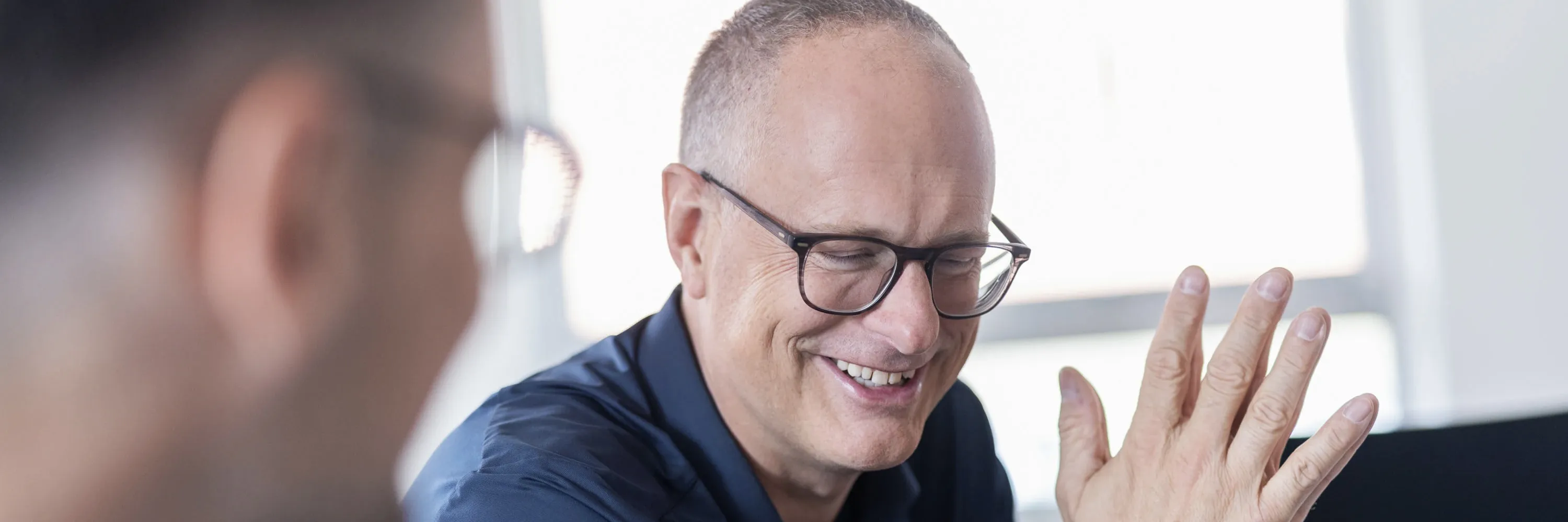 2 Personen sitzen in einem hellbeleuchteten Büroraum.